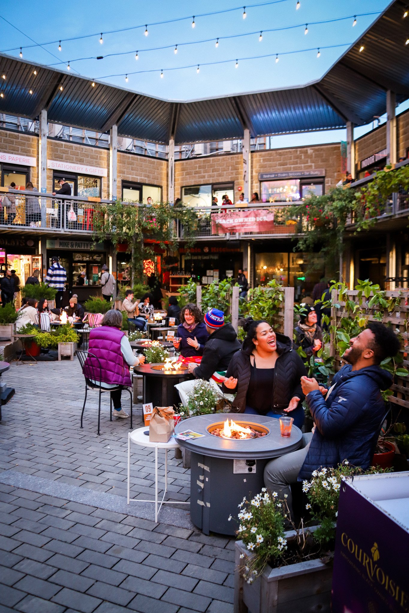 A young couple laughing around a dining table fireplace at Bow Market.